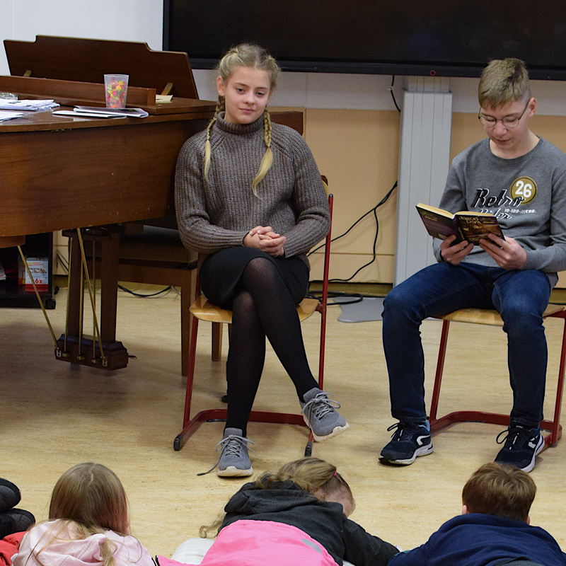 Evita Zins und Linus Wolf (beide Klasse 7b) lesen im Musikraum des Gymnasiums Kindern aus der St.-Walburga-Grundschule aus einem Kinderkrimi vor.
